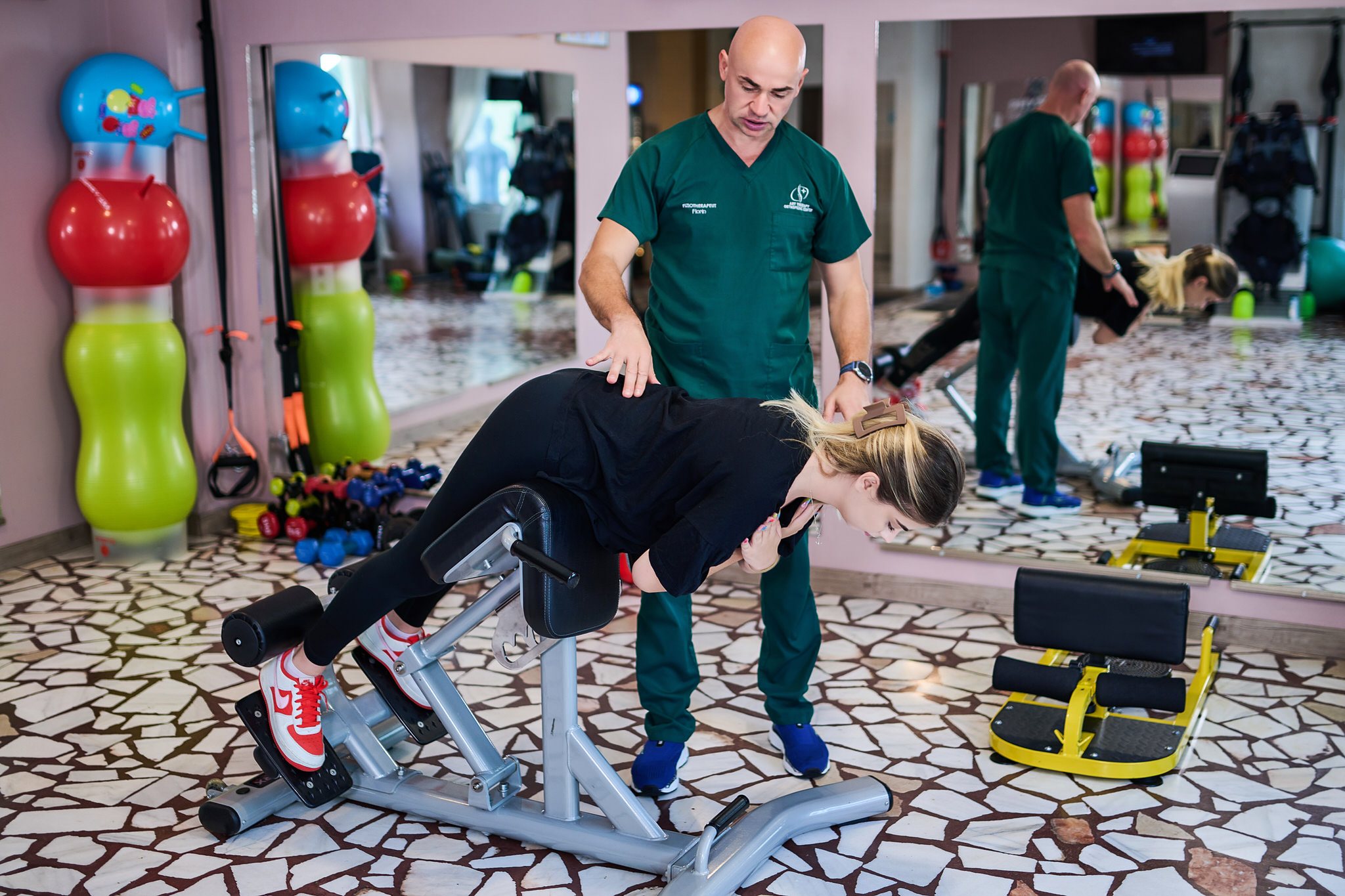 Fizioterapeut care corectează poziția spatelui la un exercițiu pe banca de hiperextensie, la centrul din Galați